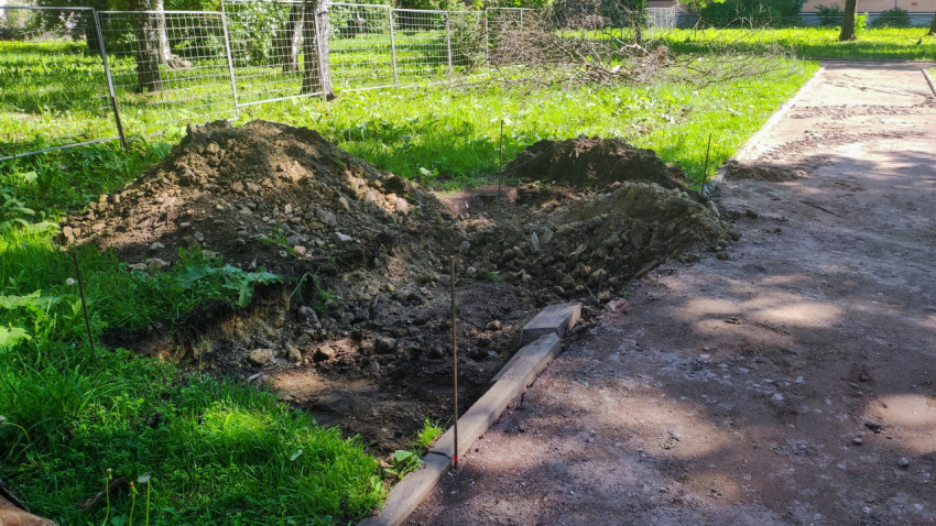 Траншея и кучи грунта у бордюра на участке ремонта пешеходной дорожки