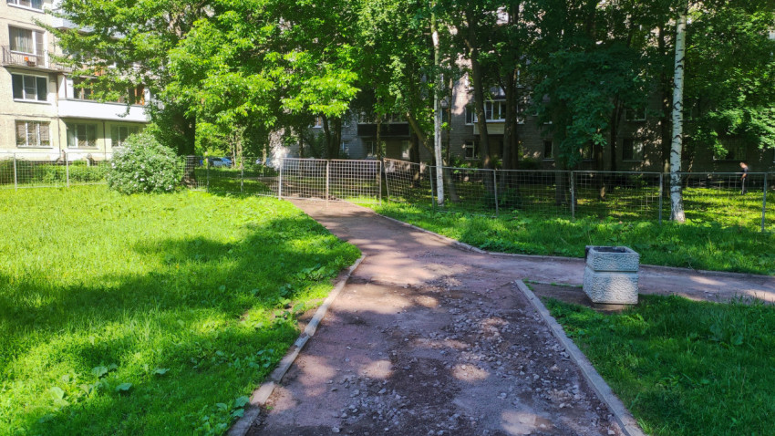 Дворовая дорожка с участком щебня и бетонной урной у временного ограждения