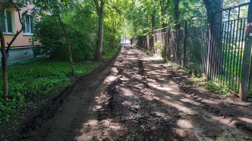Грунтовый проезд с колеями вдоль металлического забора и деревьев