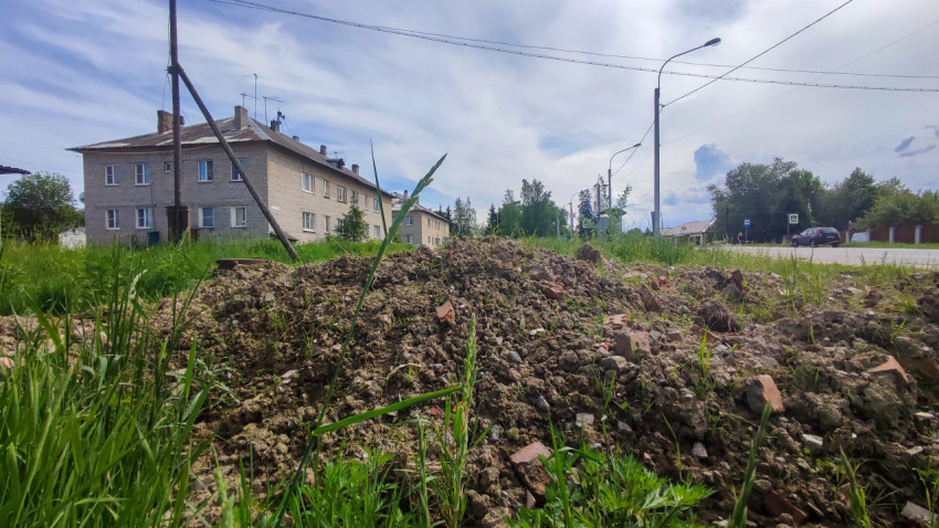 Куча грунта с обломками кирпича на траве рядом с кирпичным жилым домом и дорогой