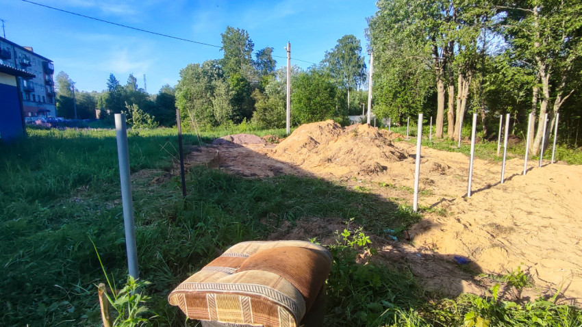 Земляные насыпи и установленные столбы на участке благоустройства рядом с деревьями