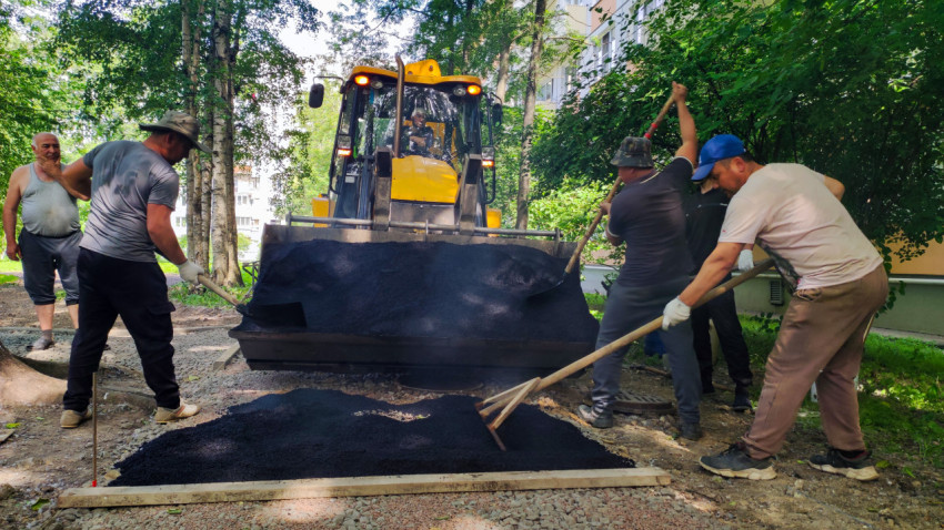 Экскаватор-погрузчик с полным ковшом асфальта и бригада дорожных рабочих