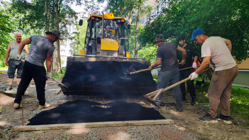 Бригада разравнивает асфальт у ковша погрузчика на дворовом проезде