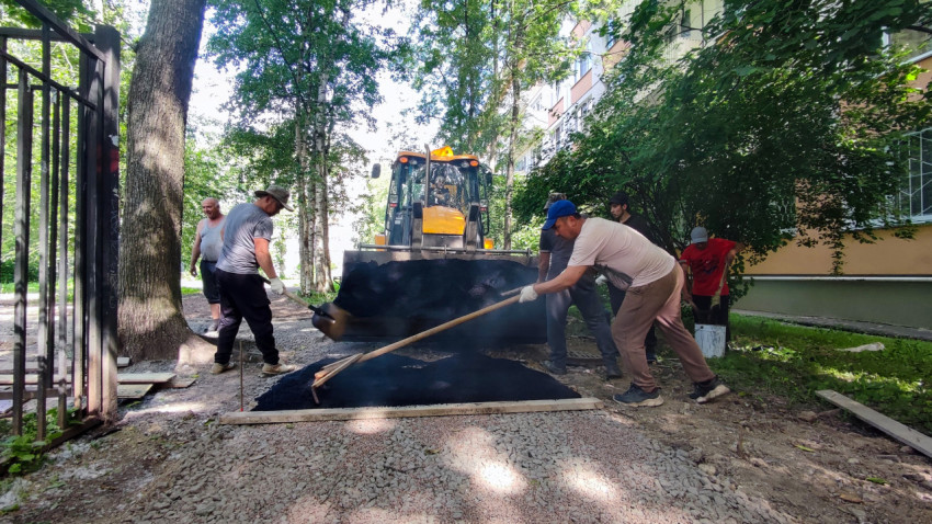 Рабочие тянут граблями асфальт по карте ремонта во дворе дома