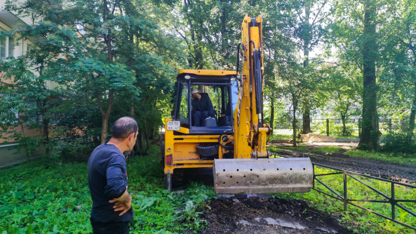 Экскаватор-погрузчик во дворе и рабочий наблюдатель у разрытого грунта