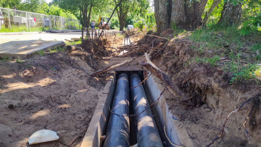 Трубопровод в открытой траншее рядом с корнями крупного дерева и техникой