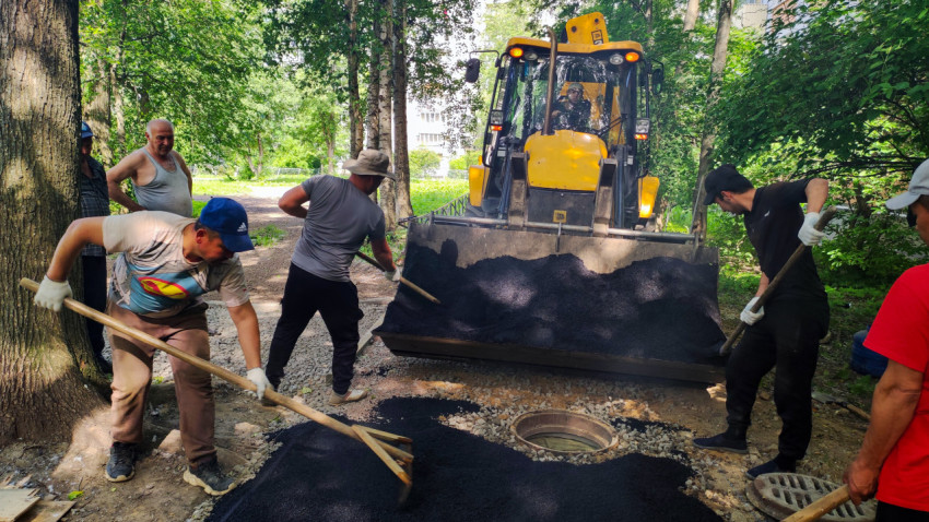 Рабочий разравнивает асфальт граблями у открытого люка на дворовом проезде