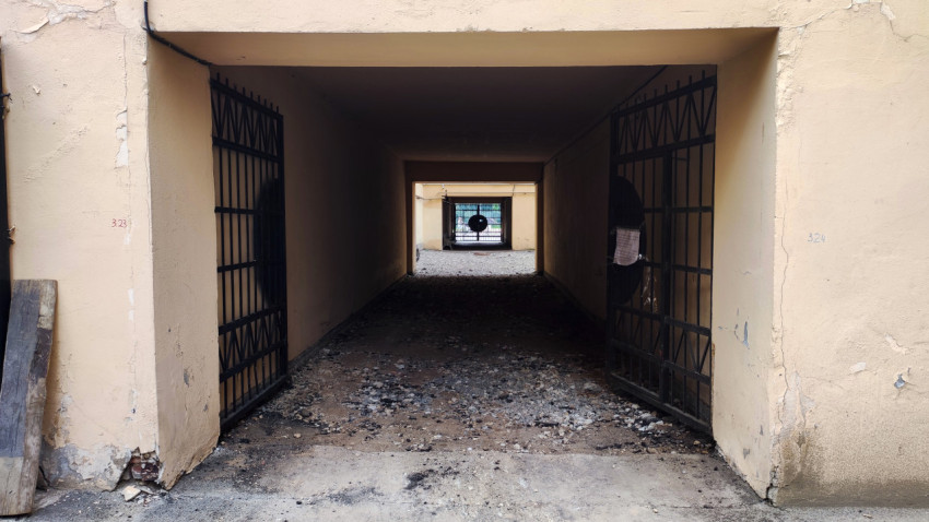 Арочный тоннель-подворотня с открытыми решётчатыми воротами и гравийным покрытием