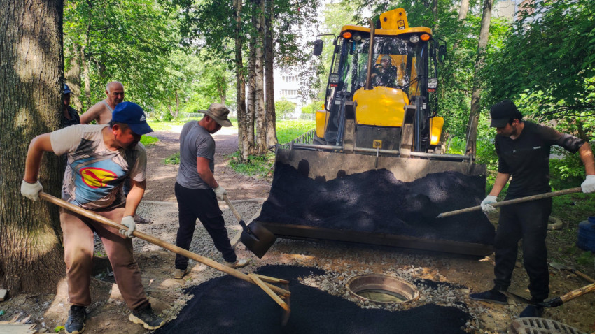 Укладка асфальта лопатой и граблями возле открытого колодца под ковшом погрузчика