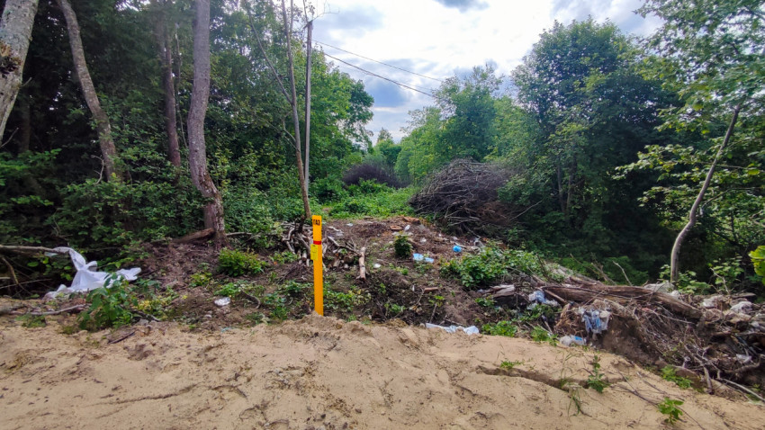 Маркерный столбик «ГАЗ» у обрыва с поваленными ветками и мусором в лесу