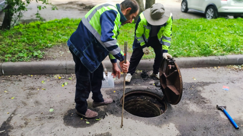 Рабочие коммунальной службы осматривают открытый люк и инструменты на дворовой дороге
