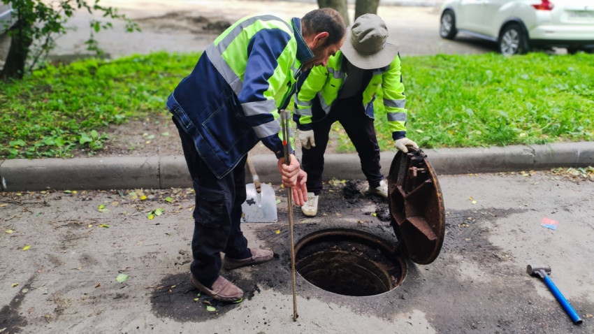 Два работника коммунальной службы осматривают открытый канализационный люк на проезжей части