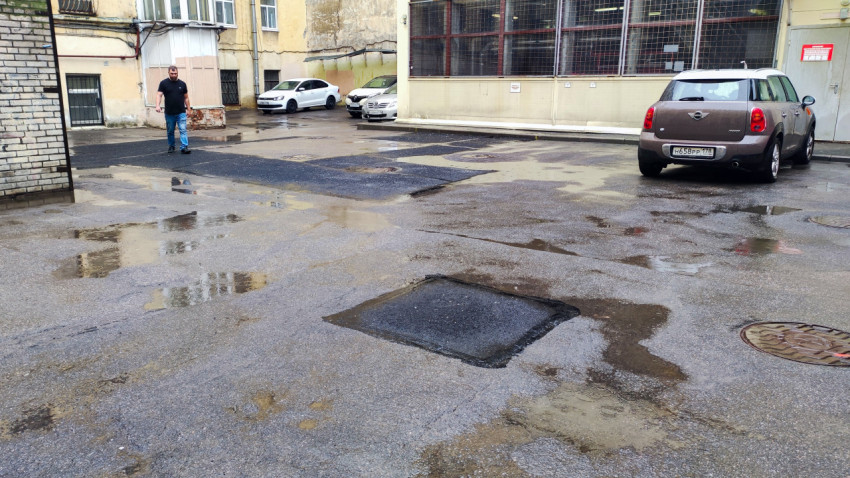 Мокрый асфальт во дворе с ремонтными заплатками, лужами и припаркованным автомобилем Mini