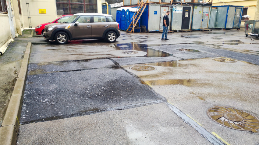 Мокрый двор с лужами, люками и строительными бытовками рядом с припаркованными машинами