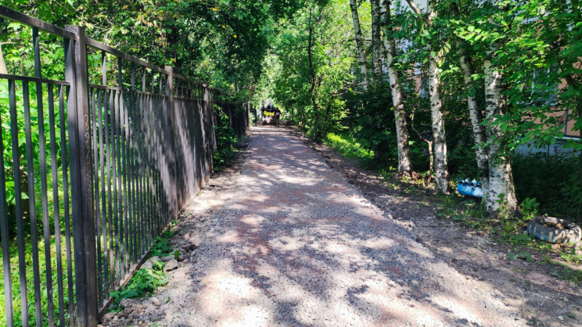 Щебеночная дорожка вдоль забора в зеленой зоне с техникой вдали