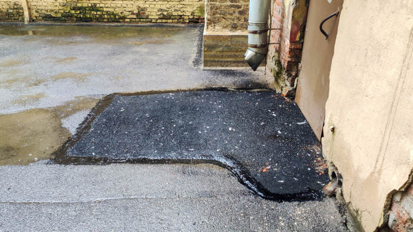 Заплатка свежего асфальта у стены здания рядом с водосточной трубой