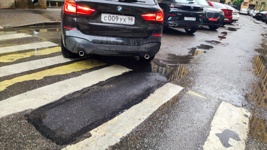 Мокрая «зебра» с заплаткой асфальта и автомобилями на парковке после дождя