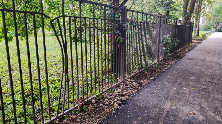 Деформированная секция металлического забора вдоль тротуара во дворе