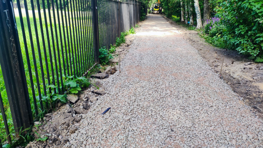 Щебеночная пешеходная дорожка в процессе устройства вдоль металлического забора и берез