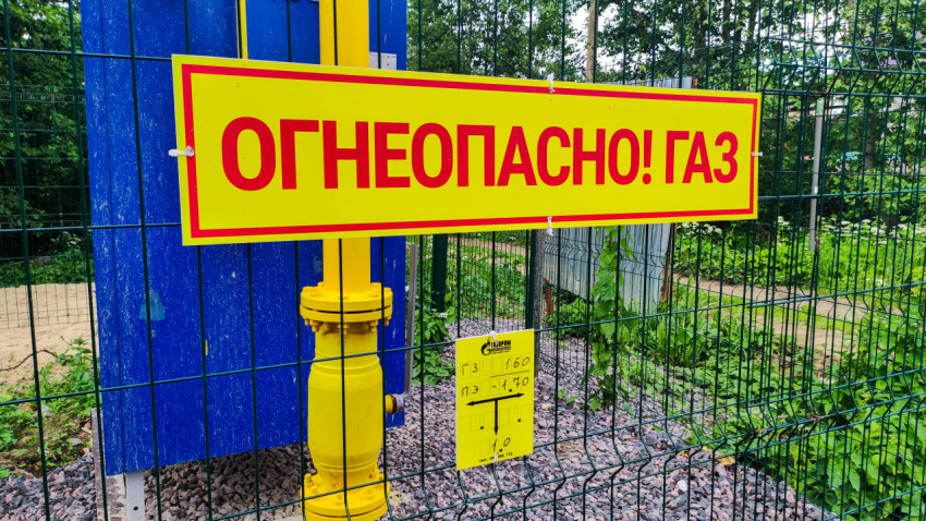 Крупный план знака «Огнеопасно! Газ» и газовой арматуры за сеткой ограждения