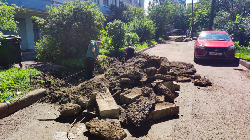 Рабочие с лопатами на раскопке у бордюра и куча демонтированного бетона на дворовой дороге