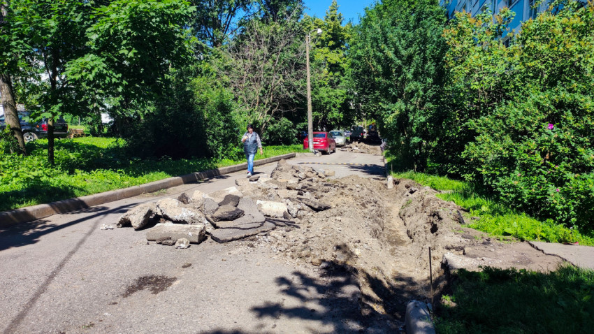 Разборка асфальта и траншея вдоль бордюра на дворовой дороге среди деревьев
