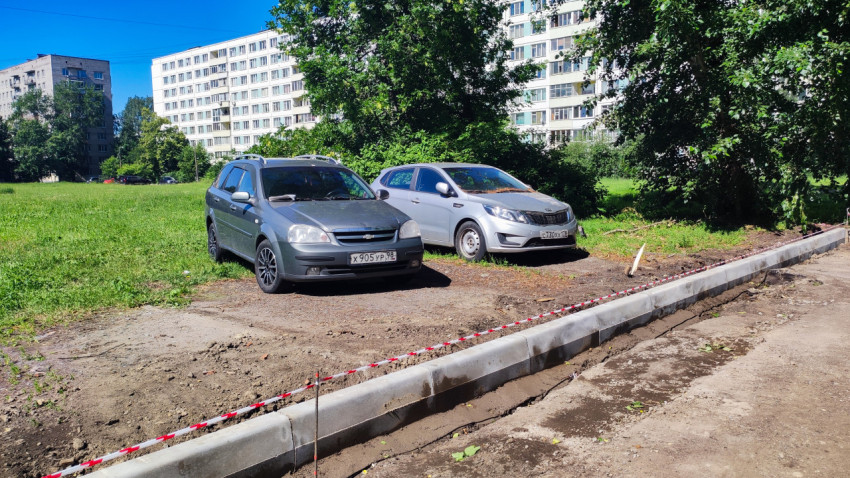 Новый бордюр с сигнальной лентой вдоль грунтовой полосы рядом с припаркованными автомобилями и жилыми домами