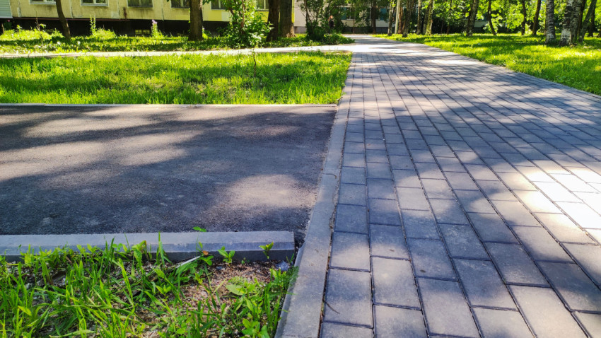 Стык асфальта и тротуарной плитки на пешеходной дорожке в зелёном дворе