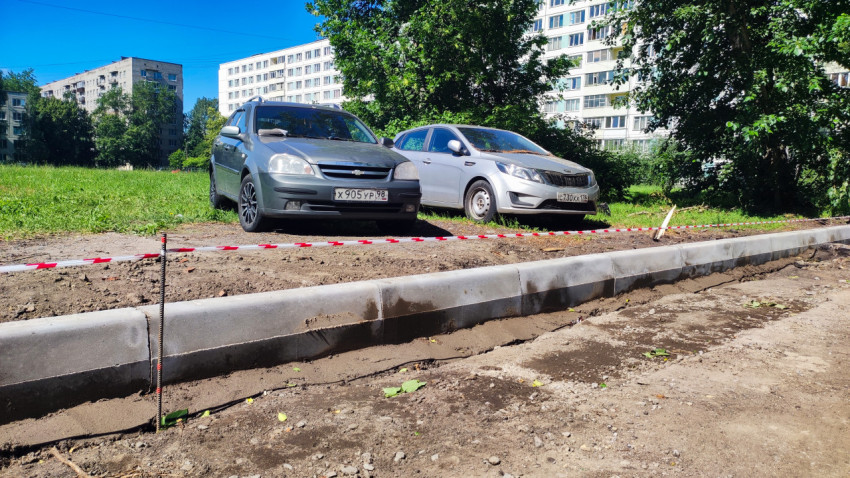 Низкий ракурс нового бордюра и сигнальной ленты на фоне дворовой парковки и многоэтажных домов