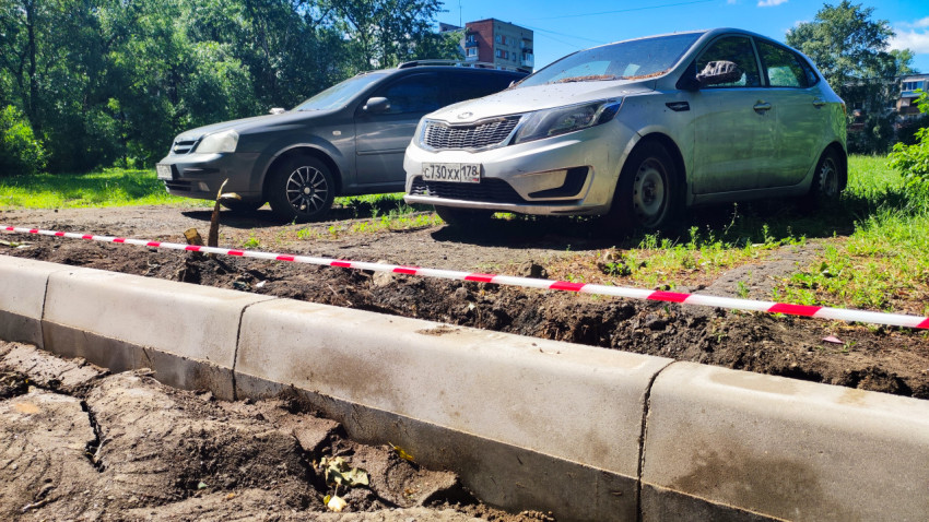 Крупный план бордюрного камня и сигнальной ленты рядом с припаркованными автомобилями на грунтовой площадке