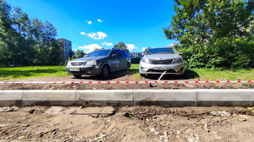 Два припаркованных автомобиля у свежего бордюра и ограждения ремонтной зоны