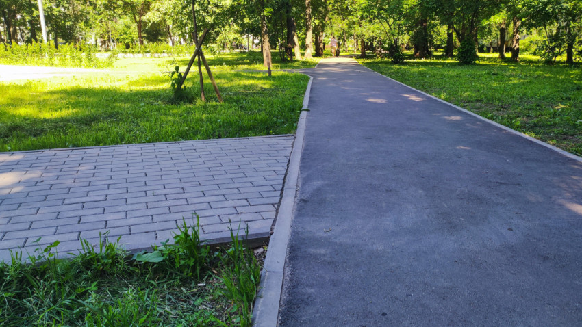 Асфальтовая дорожка с бордюром рядом с площадкой из тротуарной плитки в парке