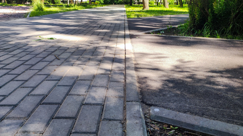 Стык дорожек из тротуарной плитки и асфальта с бордюром в парке