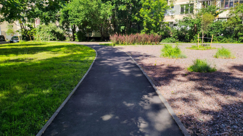 Изогнутая асфальтовая дорожка с бордюром между газоном и каменной мульчей у жилых домов