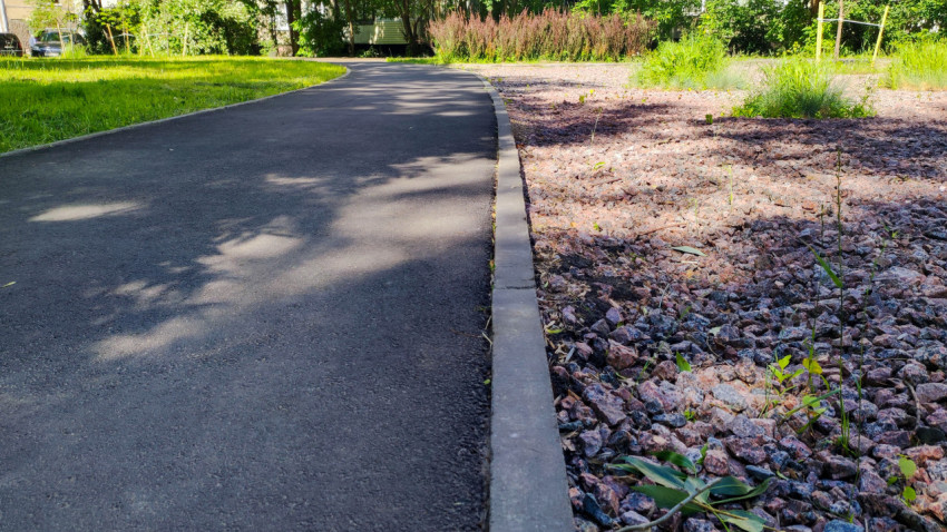 Низкий ракурс бордюра вдоль изогнутой асфальтовой дорожки рядом с каменной отсыпкой