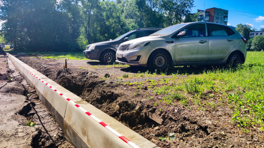 Низкий ракурс припаркованных автомобилей у нового бордюра и траншеи с сигнальной лентой