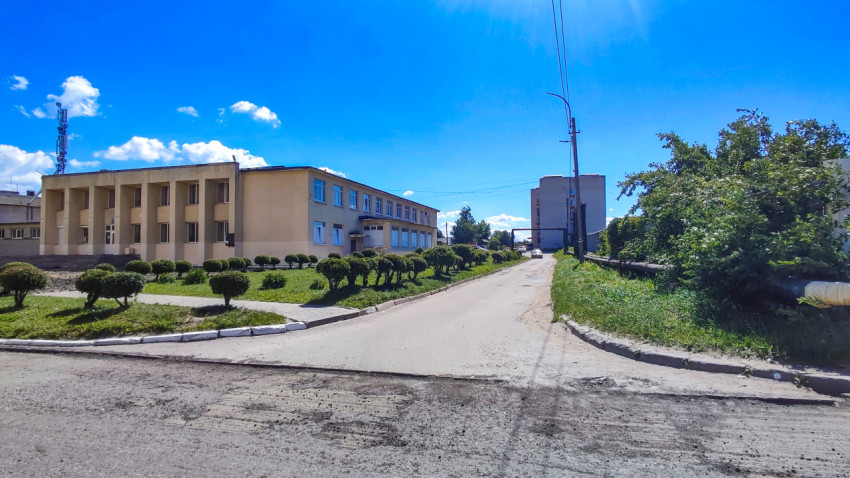 Поворот дороги у административного здания с клумбами и низкими кустарниками