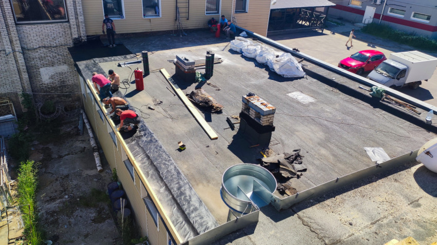 Кровельная площадка во время ремонта с газовыми баллонами, рулонами и рабочими у парапета