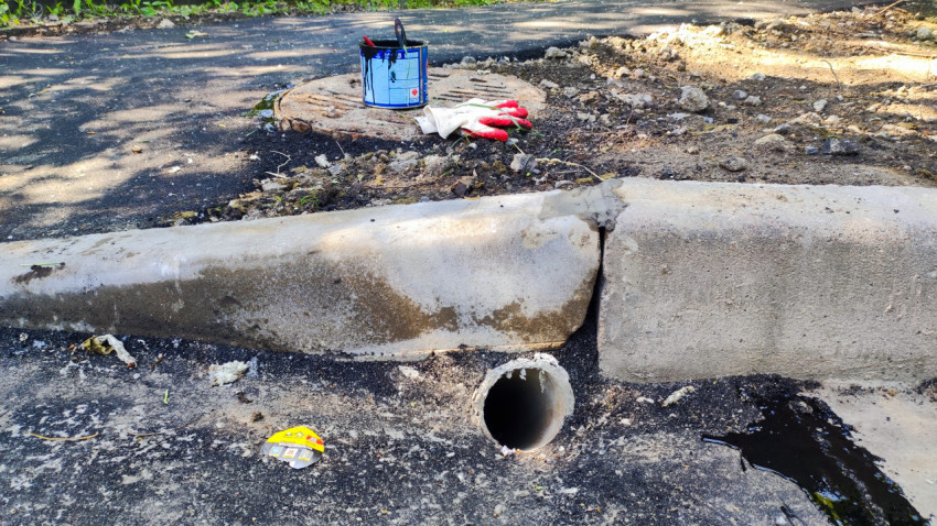 Дренажная труба под бордюром и следы водоотвода на асфальте