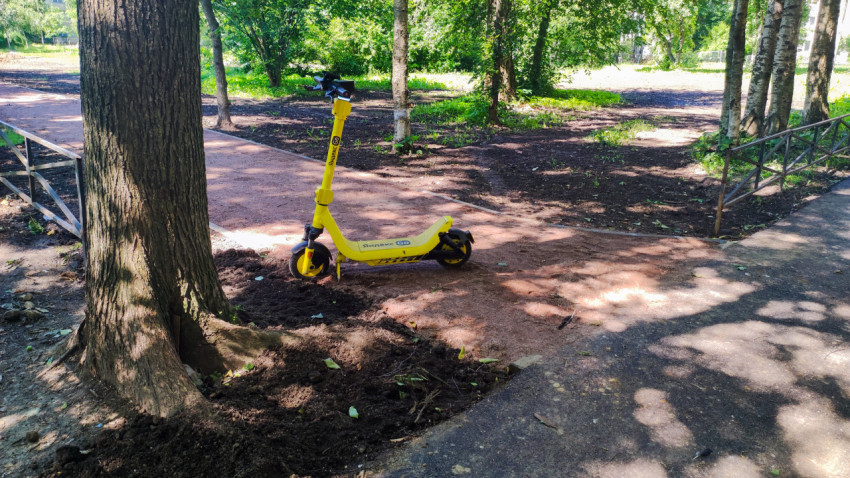 Арендный электросамокат Яндекс Go на пешеходной дорожке в зелёном сквере