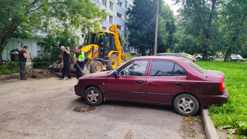 Экскаватор-погрузчик JCB и рабочие выполняют земляные работы рядом с припаркованным седаном