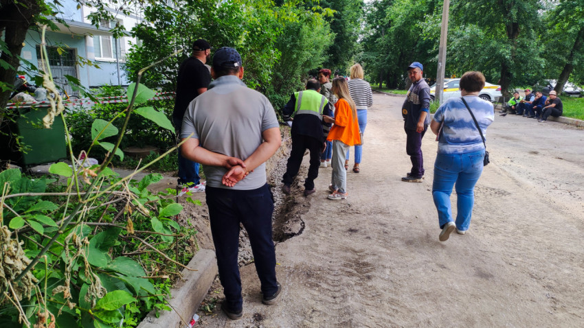 Группа рабочих и жителей осматривает край проезда у подъезда жилого дома