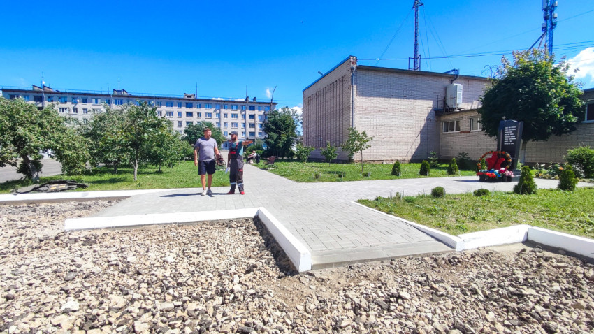 Новая пешеходная дорожка из плитки у здания рядом с памятным знаком и цветами