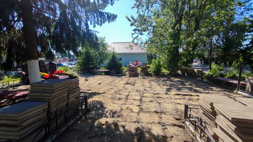 Демонтированная тротуарная плитка и штабели плит на участке благоустройства среди деревьев