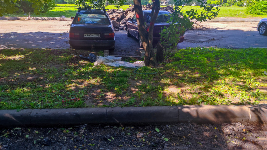 Газон у бордюра с припаркованным автомобилем и пятнами тени от деревьев