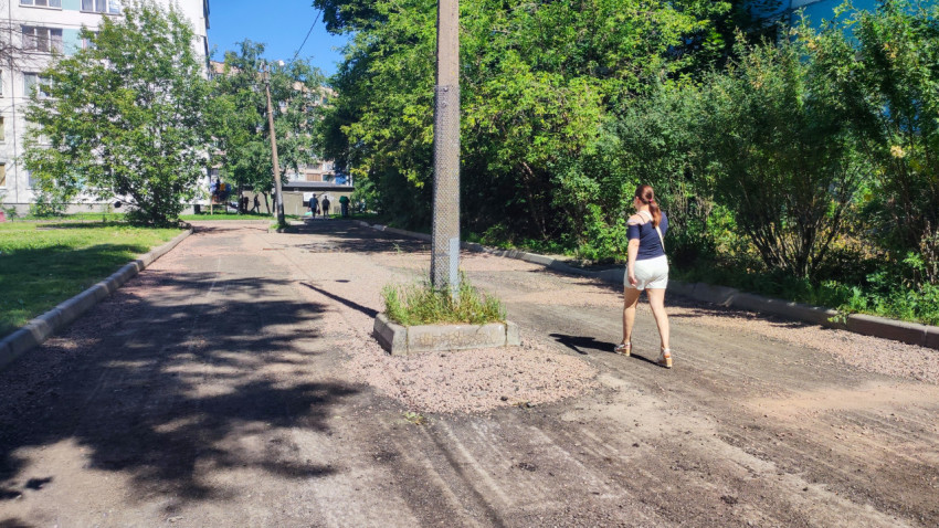 Дворовая дорожка со снятым и стрескавшимся асфальтом, отсыпкой щебня и пешеходом у жилых домов