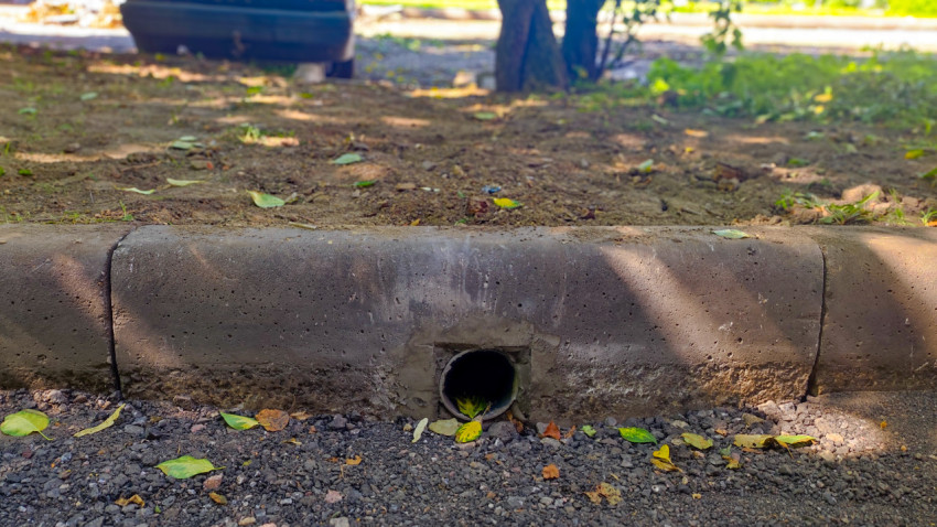 Дренажная труба в бетонном бордюре на краю дворового проезда