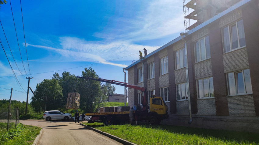 Автокран-манипулятор подаёт паллеты на крышу кирпичного здания