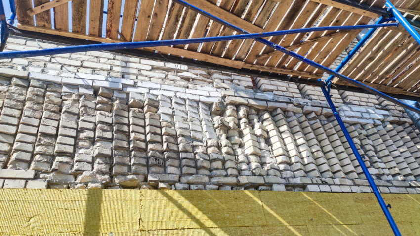 Повреждённая кирпичная кладка под строительными лесами и плиты утеплителя