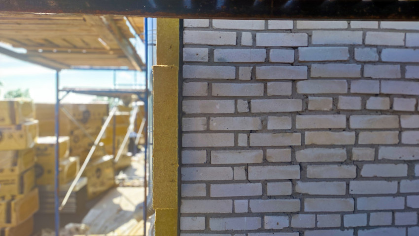 Кирпичная стена с вертикальной полосой утеплителя на строительных лесах
